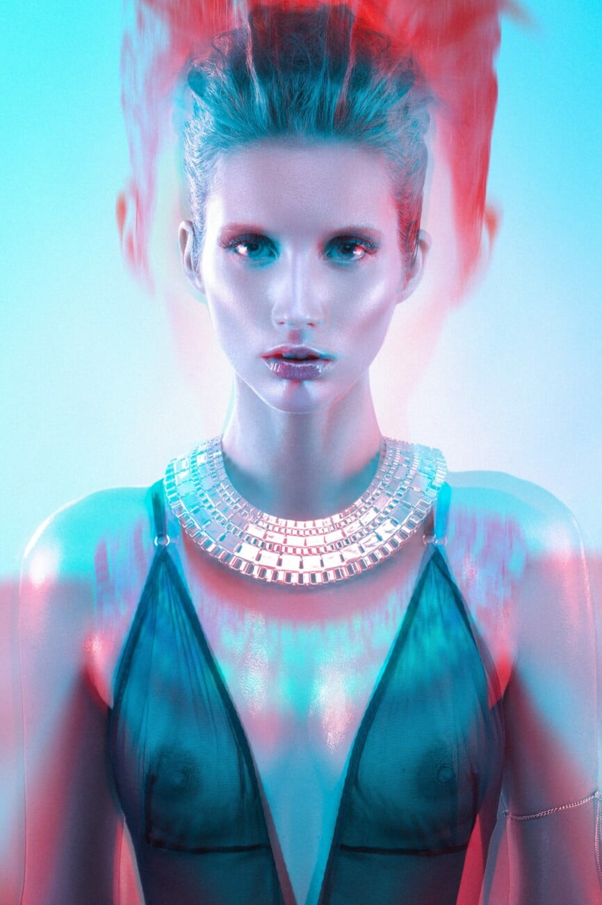Beautiful dynamic portrait of model Adeline Petit adorned with stunning jewelry and wearing a sheer top revealing her beautiful bare breasts, captured in an electric blue and red artistic image by photographer Etienne Delorme for Faust Magazine