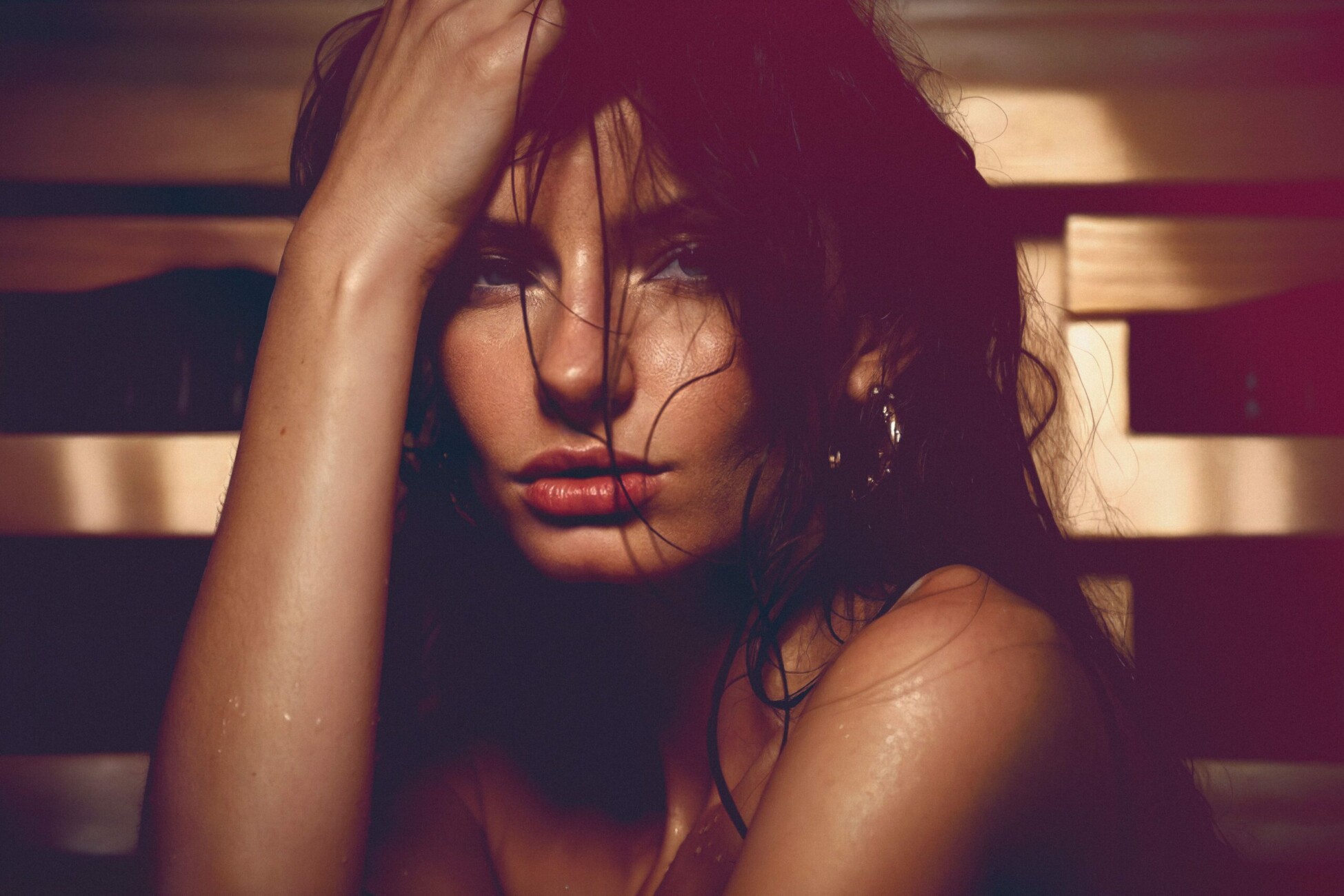 Close-up of a woman with wet hair, hand tangled in hair, looking toward the camera with moody lighting on skin.