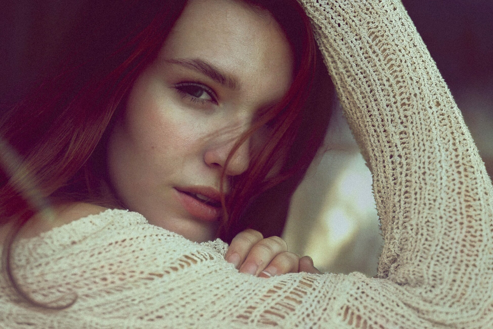 Close-up portrait of a woman with red hair, wrapped in a beige knitted shawl, looking softly toward the camera.